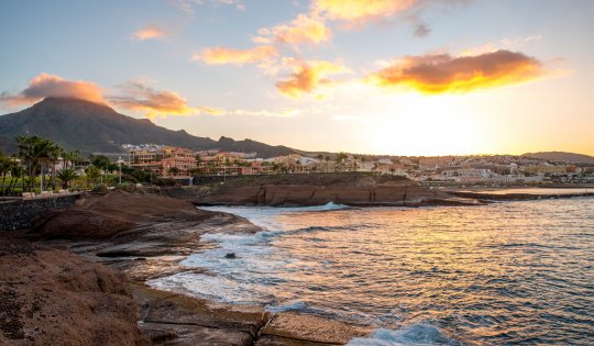 Felsige Küste im Ferienort Los Cristianos bei Sonnenaufgang auf der Insel Teneriffa in Spanien