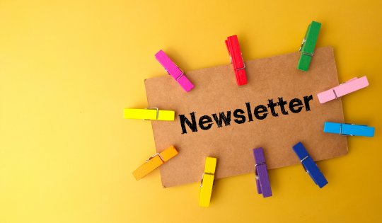 Colored wooden clips and brown card written with text Newsletter on yellow background.