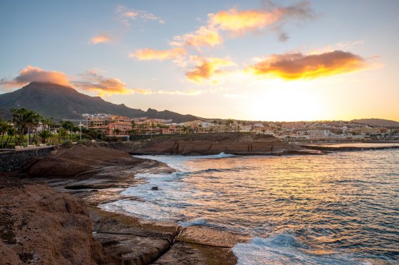 Felsige Küste im Ferienort Los Cristianos bei Sonnenaufgang auf der Insel Teneriffa in Spanien