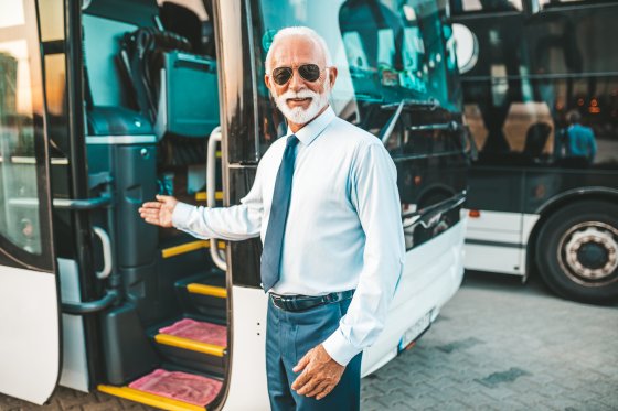 Mature beard bus driver standing in front of bus..